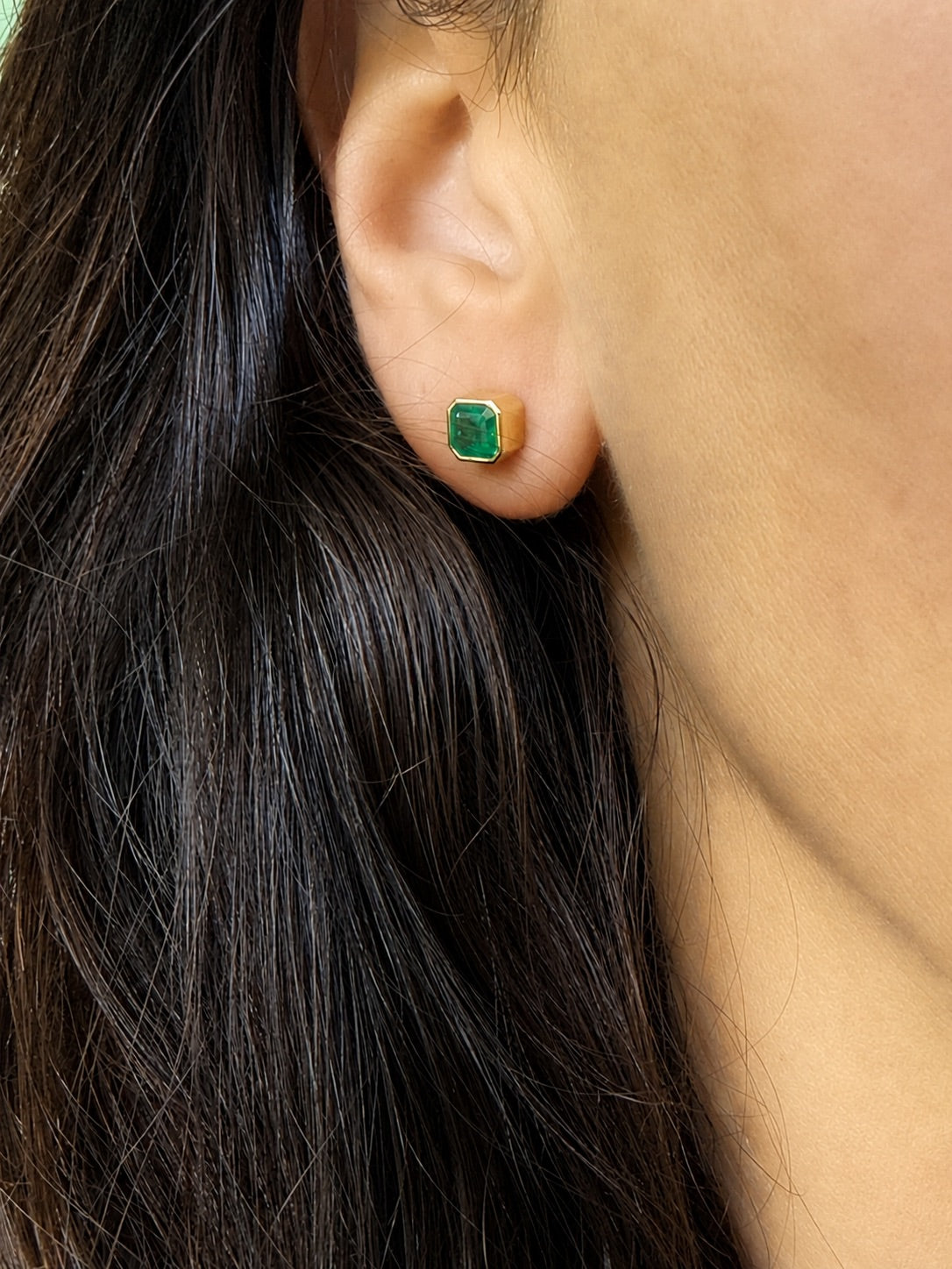 Asscher-cut Colombian emerald stud earring in 18K yellow gold, close view of the bezel setting