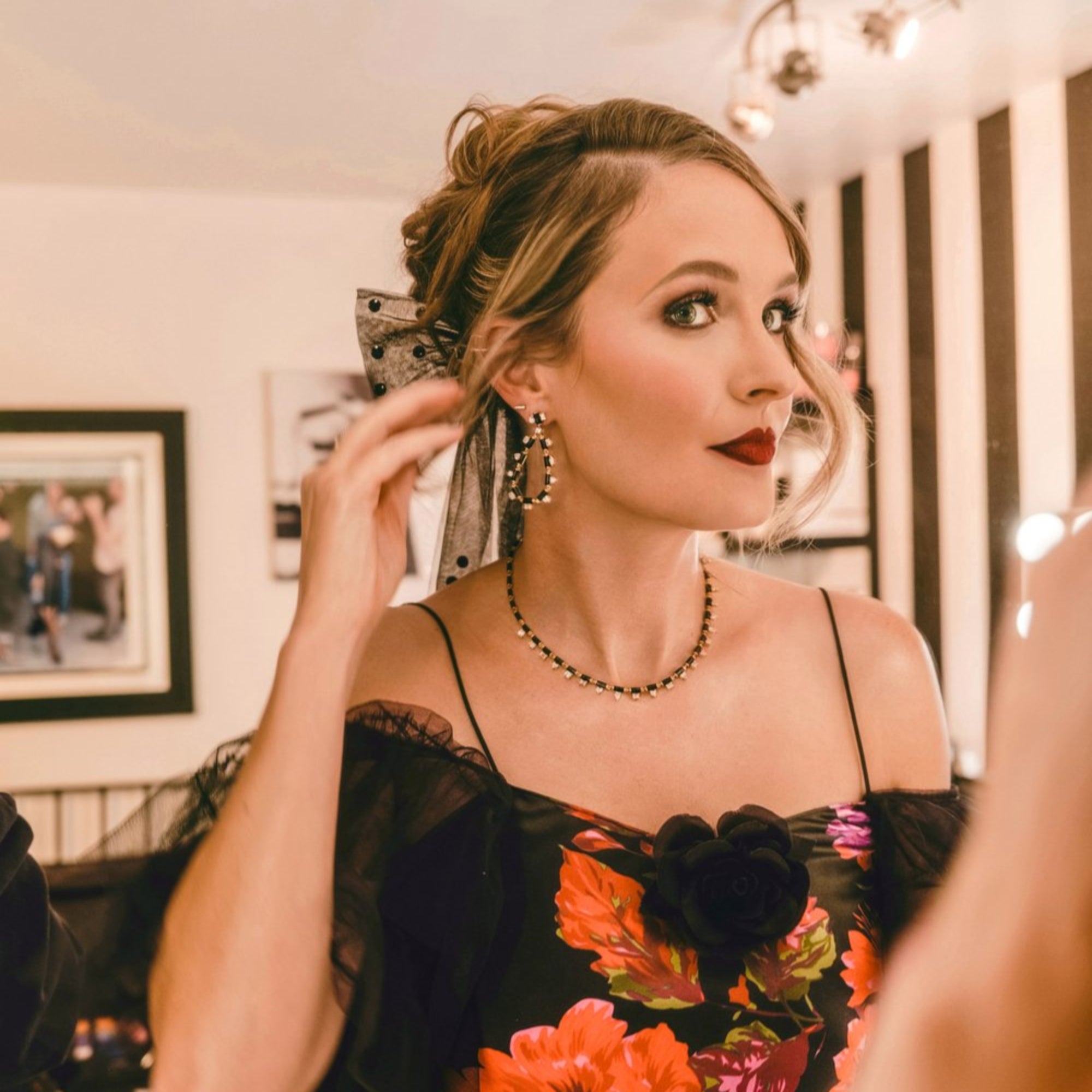 Courtney McBroom wearing black onyx and mixed-shaped diamond teardrop earrings, paired with a black floral dress and matching black gemstone necklace in a softly lit dressing room.