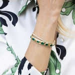Exquisite 14K yellow gold bangle featuring seven bezel-set emeralds in mixed shapes totaling 10 carats, creating a bold yet refined statement of elegance and color.