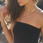 Round bezel set sapphire tennis bracelet, layered with other gold and gemstone bracelets, worn on the wrist.