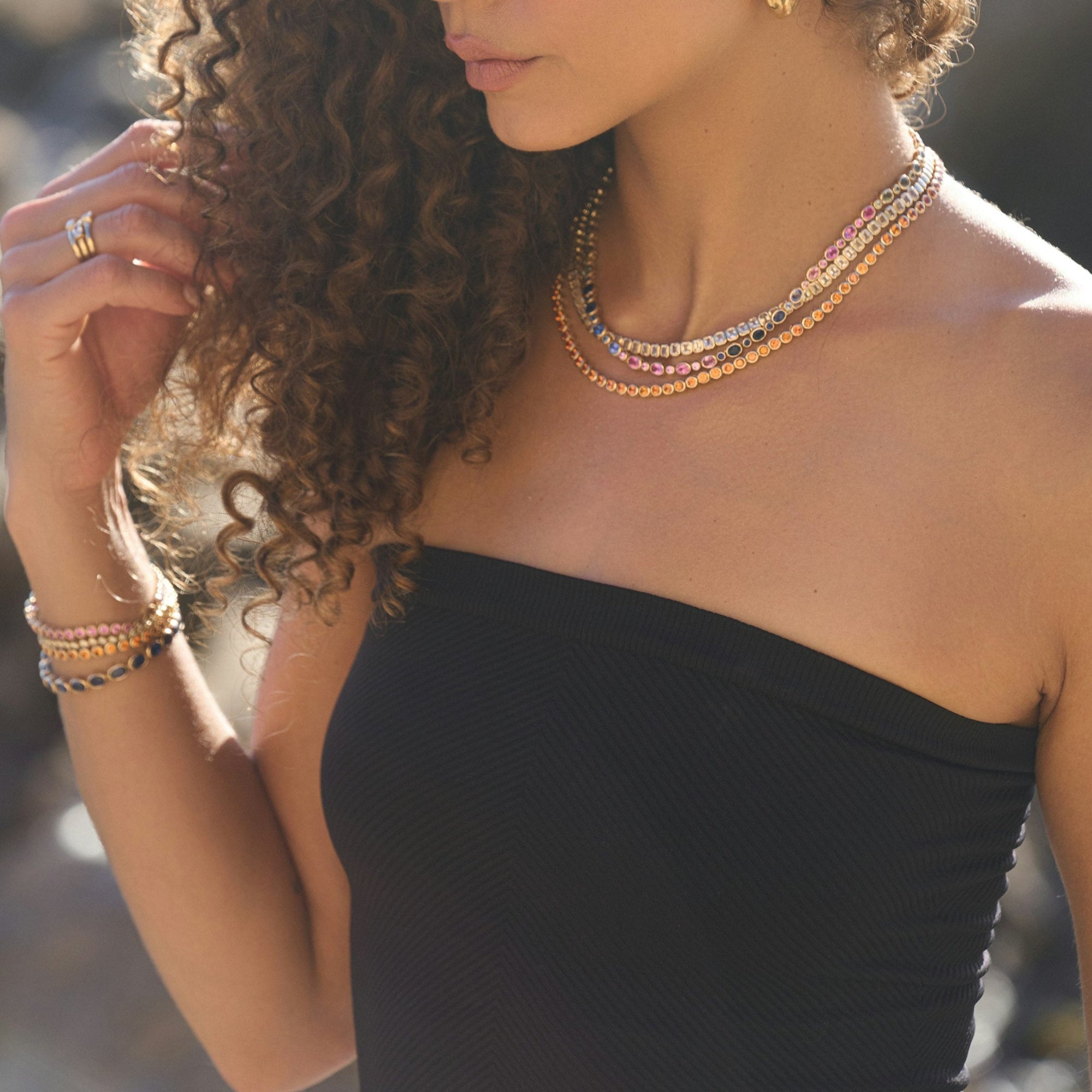 Round bezel set sapphire tennis bracelet, layered with other gold and gemstone bracelets, worn on the wrist.