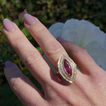 Art Deco-inspired 18K yellow gold ring featuring a radiant marquise-cut pink tourmaline encircled by a sparkling double diamond halo, meticulously crafted for timeless elegance and sophistication. On right ring finger.