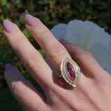 Art Deco-inspired 18K yellow gold ring featuring a radiant marquise-cut pink tourmaline encircled by a sparkling double diamond halo, meticulously crafted for timeless elegance and sophistication. On right ring finger.