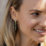 Captivating double hoop earrings featuring shimmering diamonds and vibrant emeralds in a double huggie design, accentuated by delicate dangling chains for a blend of classic sophistication and modern allure. On model in right ear. 