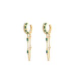 Captivating double hoop earrings featuring shimmering diamonds and vibrant emeralds in a double huggie design, accentuated by delicate dangling chains for a blend of classic sophistication and modern allure. Side view, close up.