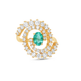 Stunning 14K yellow gold spiral ring featuring a vivid oval-cut emerald at its center, encircled by two spirals of sparkling round brilliant-cut diamonds, blending modern design with timeless elegance. Front view, close up. 