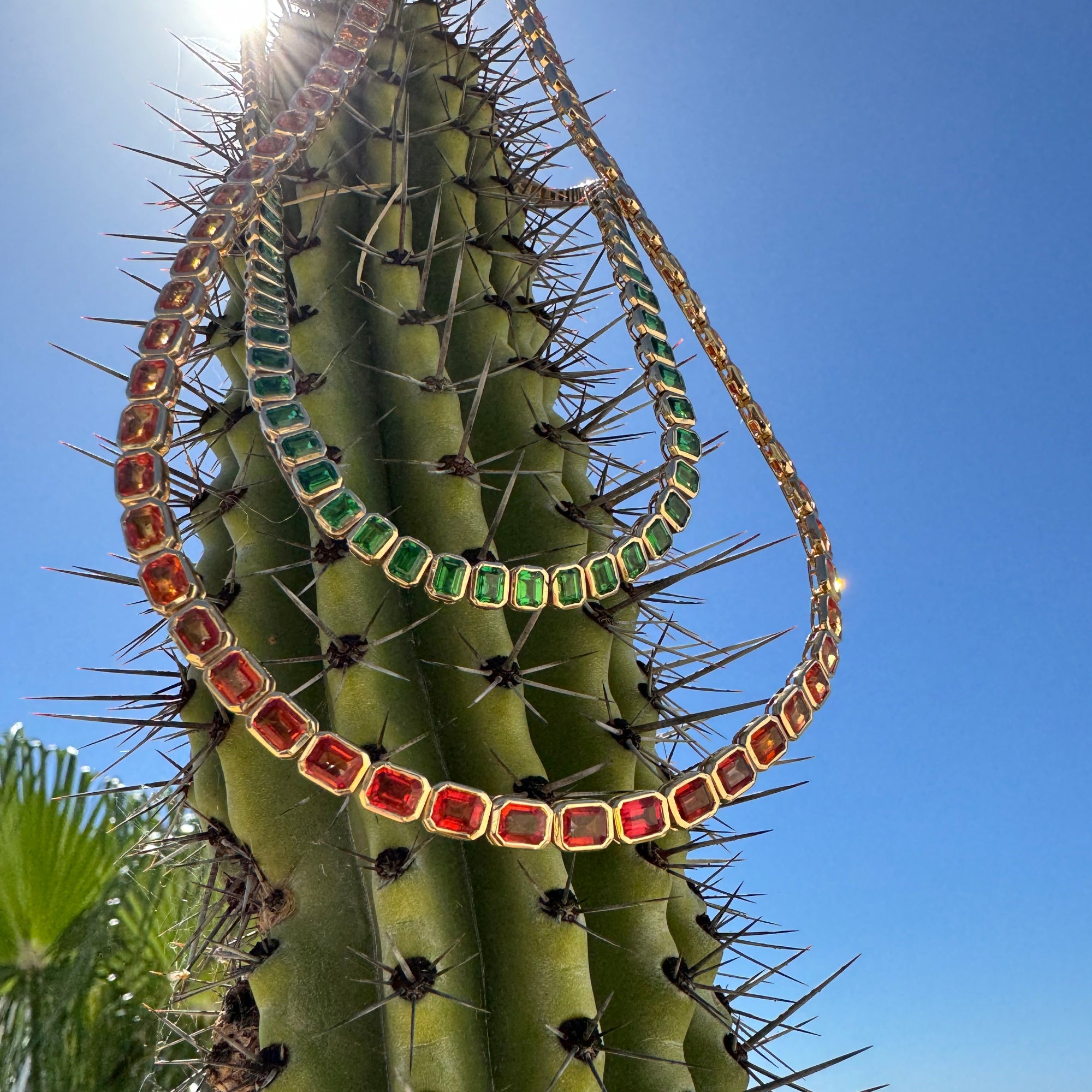 Stunning one-of-a-kind mandarin orange sapphire necklace featuring large east-west set emerald-cut sapphires, elegantly wrapped in 14K yellow gold for a bold and vibrant statement. Nature shot. 
