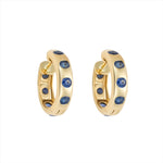 Striking 14K yellow gold huggie earrings featuring 1.79ct of vibrant blue sapphires, set in 1/2-inch wide hoops for a colorful and elegant everyday accessory.
