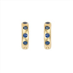 Striking 14K yellow gold huggie earrings featuring 1.79ct of vibrant blue sapphires, set in 1/2-inch wide hoops for a colorful and elegant everyday accessory.