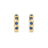 Striking 14K yellow gold huggie earrings featuring 1.79ct of vibrant blue sapphires, set in 1/2-inch wide hoops for a colorful and elegant everyday accessory.