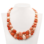Exquisite 18K yellow gold bib necklace featuring hand-carved coral gemstones in varying shapes and sizes, accented by delicately placed diamonds for added brilliance, creating a striking and timeless statement piece. Front view of necklace. 