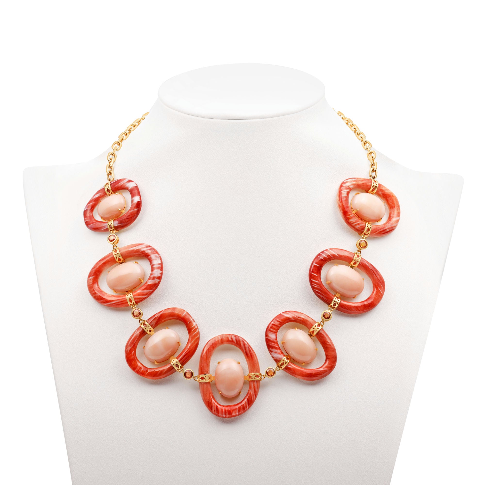 Striking 18K yellow gold link necklace featuring hand-carved orange shell links, smooth pink coral cabochons, and delicate orange sapphires, blending warm hues with masterful craftsmanship for a bold yet sophisticated statement piece. On bust.