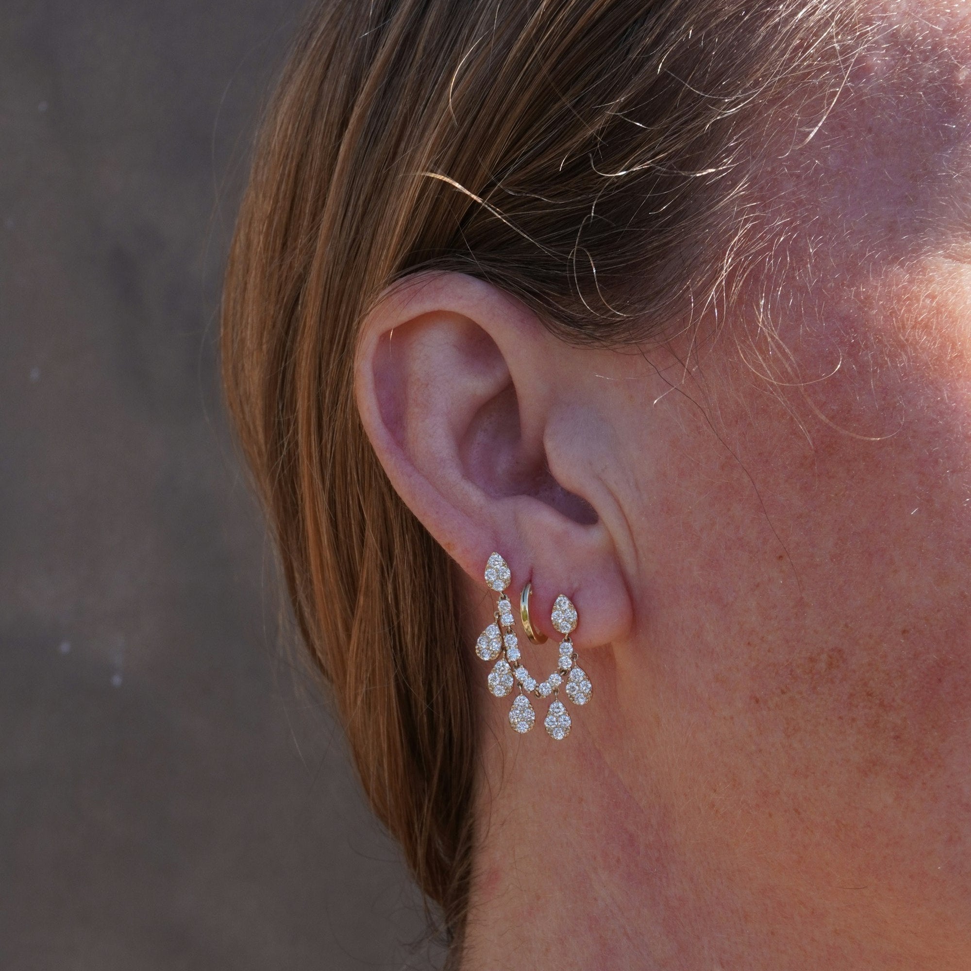 Stunning double post stud huggie earrings crafted in 14K yellow gold, featuring pear-shaped gold bead drops inlaid with sparkling pavé diamonds, creating a graceful cascade of brilliance for refined luxury. On model. 