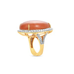Stunning 18K yellow gold statement ring featuring a captivating pear-shaped coral cabochon, elegantly framed by a halo of brilliant diamonds, blending natural warmth with luxurious sparkle. Angled, close up,
