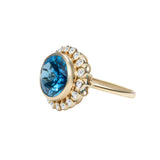 Captivating 14K yellow gold cocktail ring featuring a Swiss blue topaz surrounded by a sparkling diamond halo in a delicate anemone-inspired basket setting, offering vibrant elegance for any occasion.