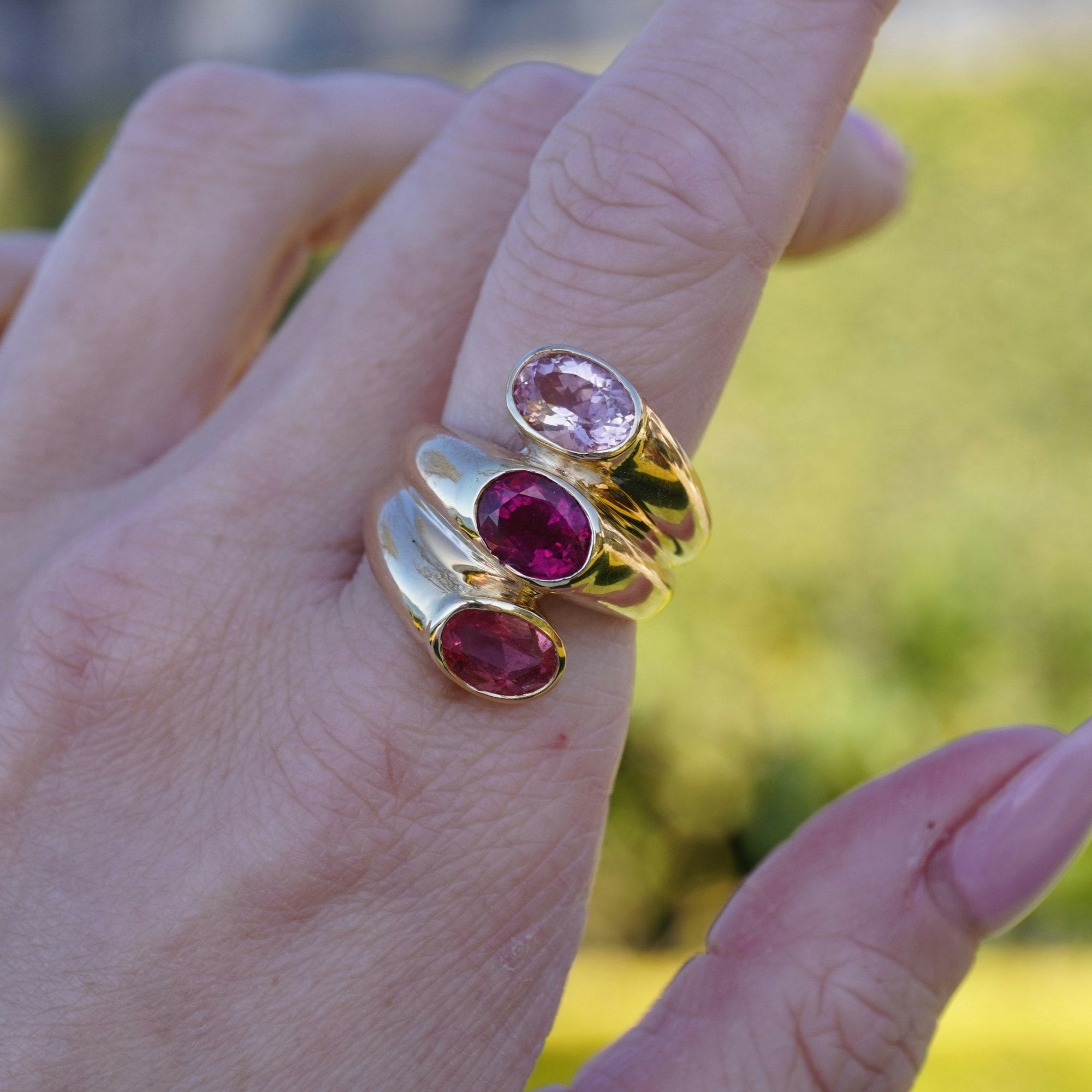 Unique 14K yellow gold statement ring featuring three bezel-set tourmaline stones in delicate shades of pink, blending elegance with bold color for a timeless look. On models left pointer finger.
