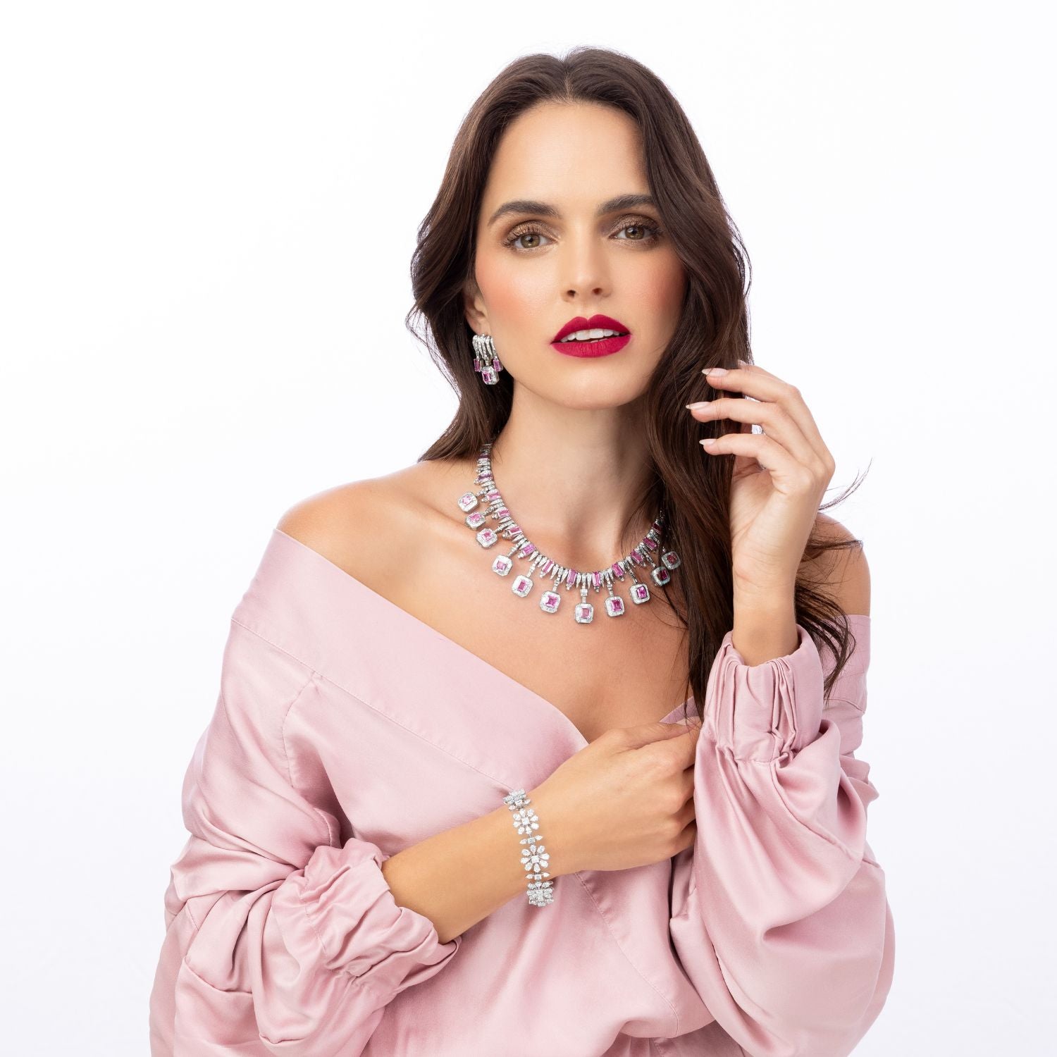 Woman wearing a pink off-shoulder top and silver jewelry on a white background