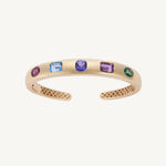 Five-stone bangle in 14K yellow gold with emerald, purple sapphire, iolite, Swiss blue topaz and pink tourmaline flush-set into a polished cuff. This piece was reset in tanzanite in May 2025.