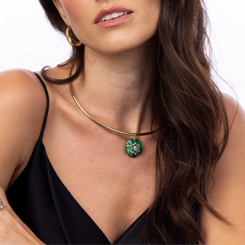Model wearing Elyzian Fleur de Charme malachite flower pendant on gold collar necklace with gold
hoop earrings
