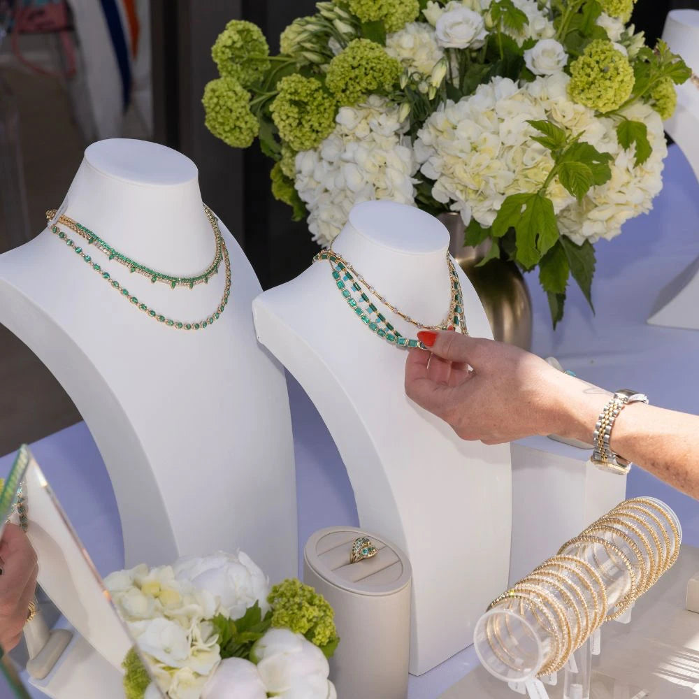Elyzian trunk show featuring emerald tennis necklaces on white displays with customer interaction