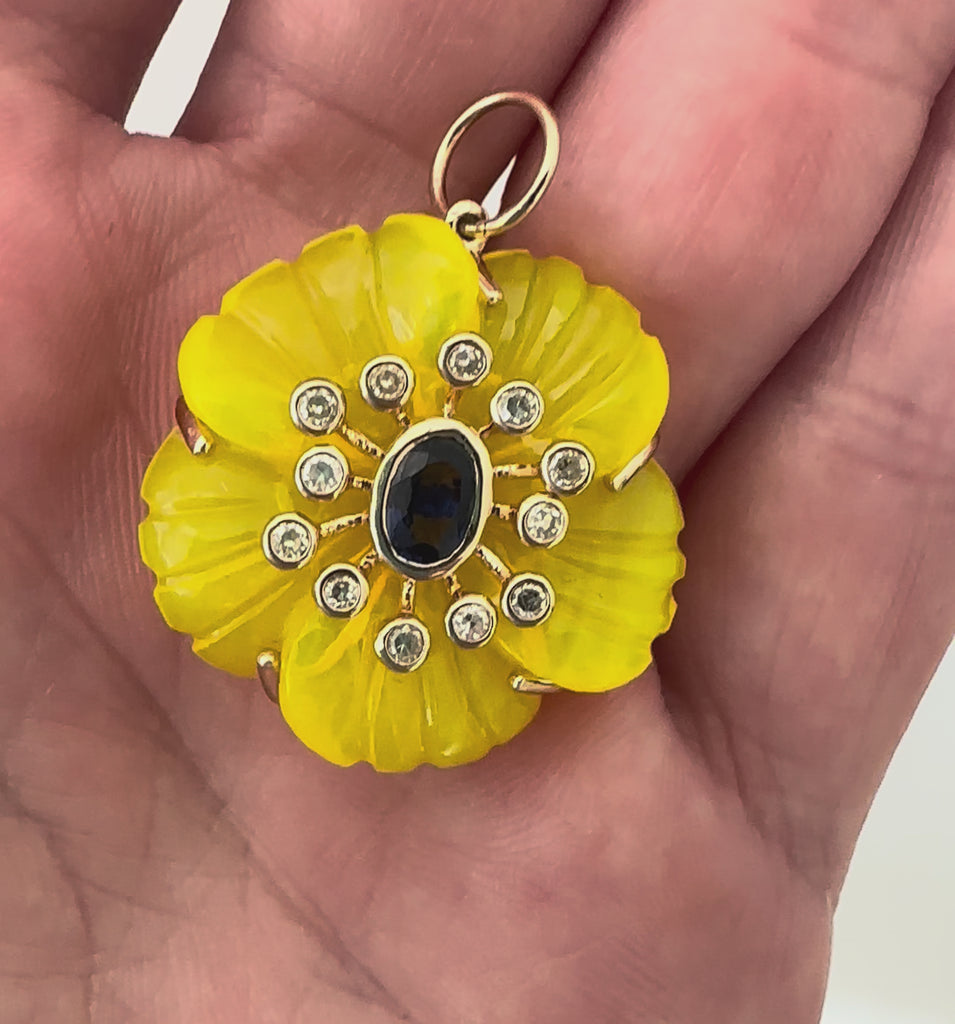 Azure Glow captures sunshine meeting ocean in one extraordinary piece. Six hand-carved yellow quartz petals, treated to achieve golden perfection, frame a faceted blue sapphire center.

At nearly 24 carats, these petals catch light like August afternoons. The 0.57-carat sapphire shows pure Ceylon blue, the kind that reminds you why sapphires remain eternal favorites. Diamonds surround this study in contrasts, adding brilliance to the joyful color story.